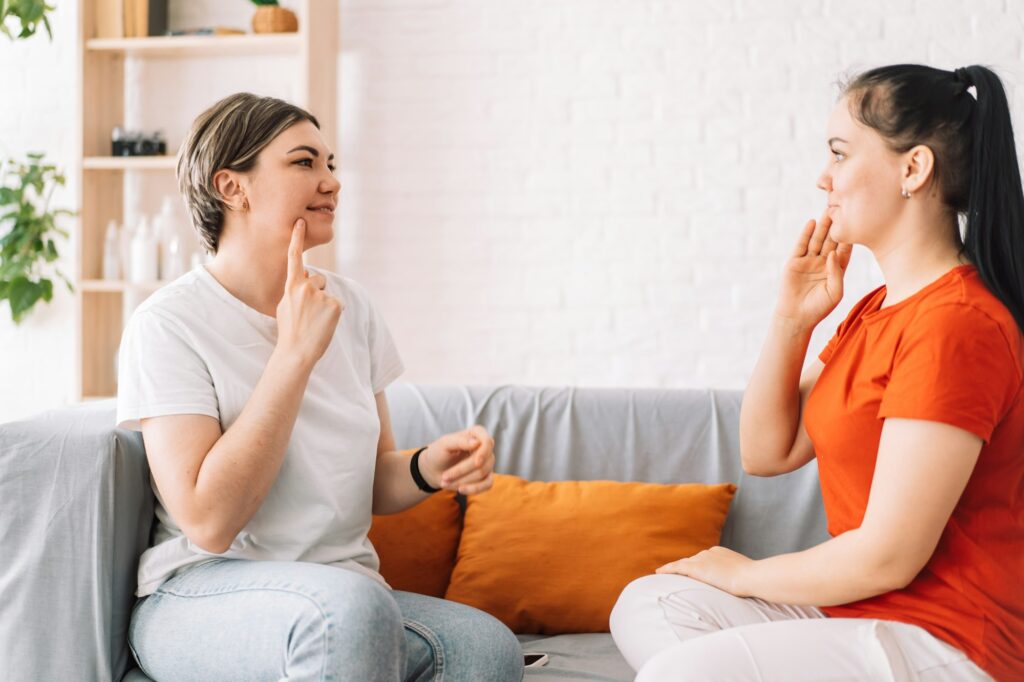 The teacher teaches the girl sign language while sitting on the couch